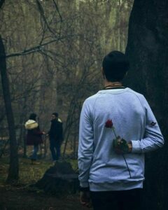 A boy is standing with a rose in his hand and he is sad